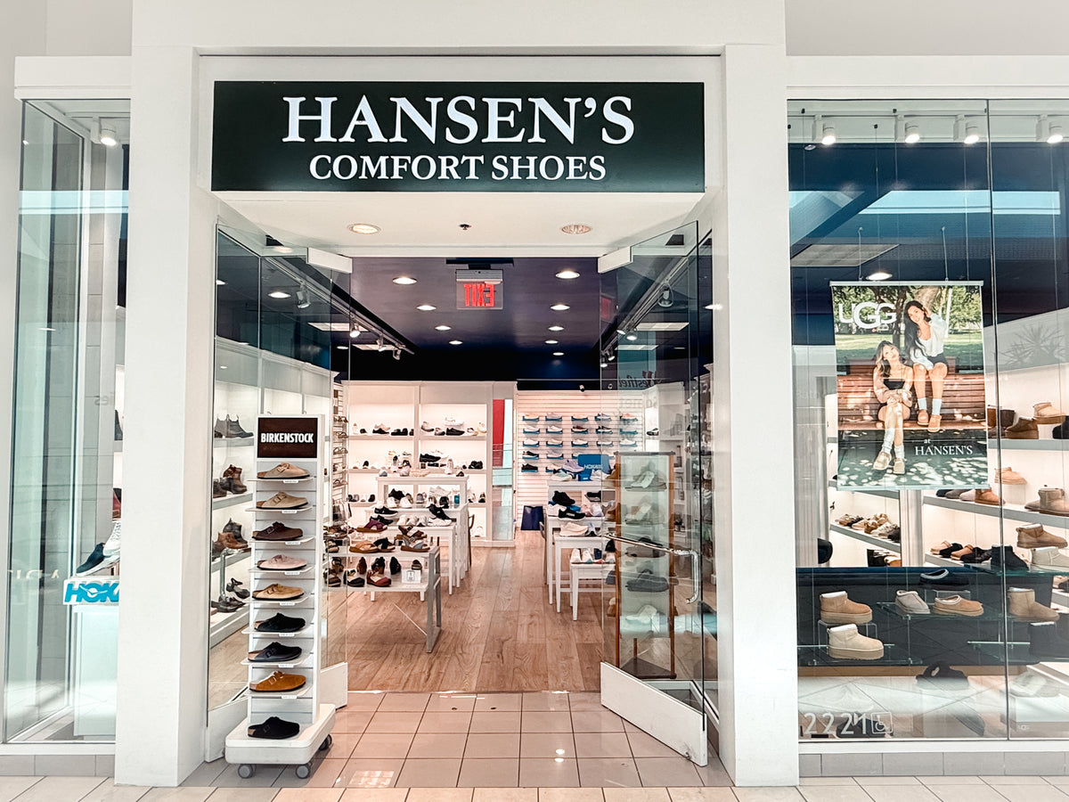 Hansen's Comfort Shoes retail store entrance with glass doors, a black sign with white lettering, and multiple shoe displays inside and on the sides.